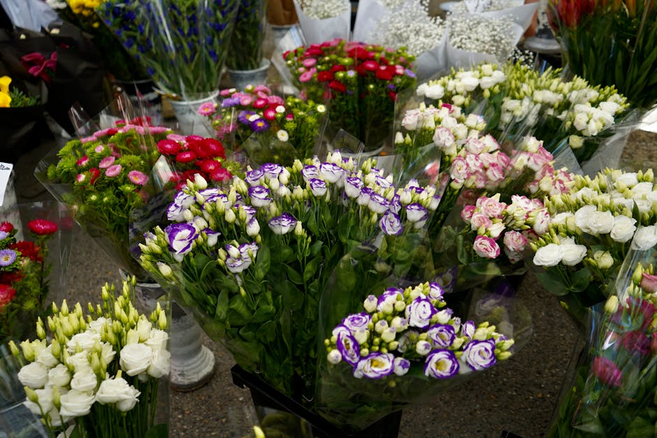 A vibrant display of fresh flowers arranged in bouquets and individual stems at a florist's shop. Prominent among them are purple and white lisianthus with delicate, ruffled petals, surrounded by clus