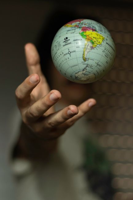 A person holding a small globe with their left hand, displaying continents such as South America, Africa, and parts of North America. The globe features bright, colorful map details and is positioned 